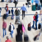 Couple embraced in a busy airport while people are in motion blu